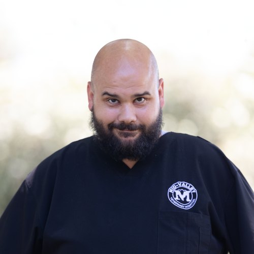 John, a Registered Veterinary Technician at Mid-Valley Veterinary Hospital, smiling outdoors in Mid-Valley scrubs.