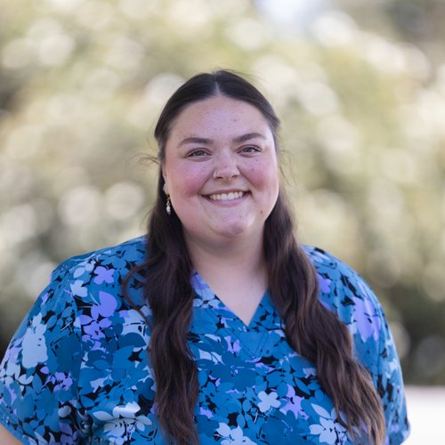 Madison, a Customer Service Representative at Mid-Valley Veterinary Hospital, smiling outdoors in blue floral scrubs.